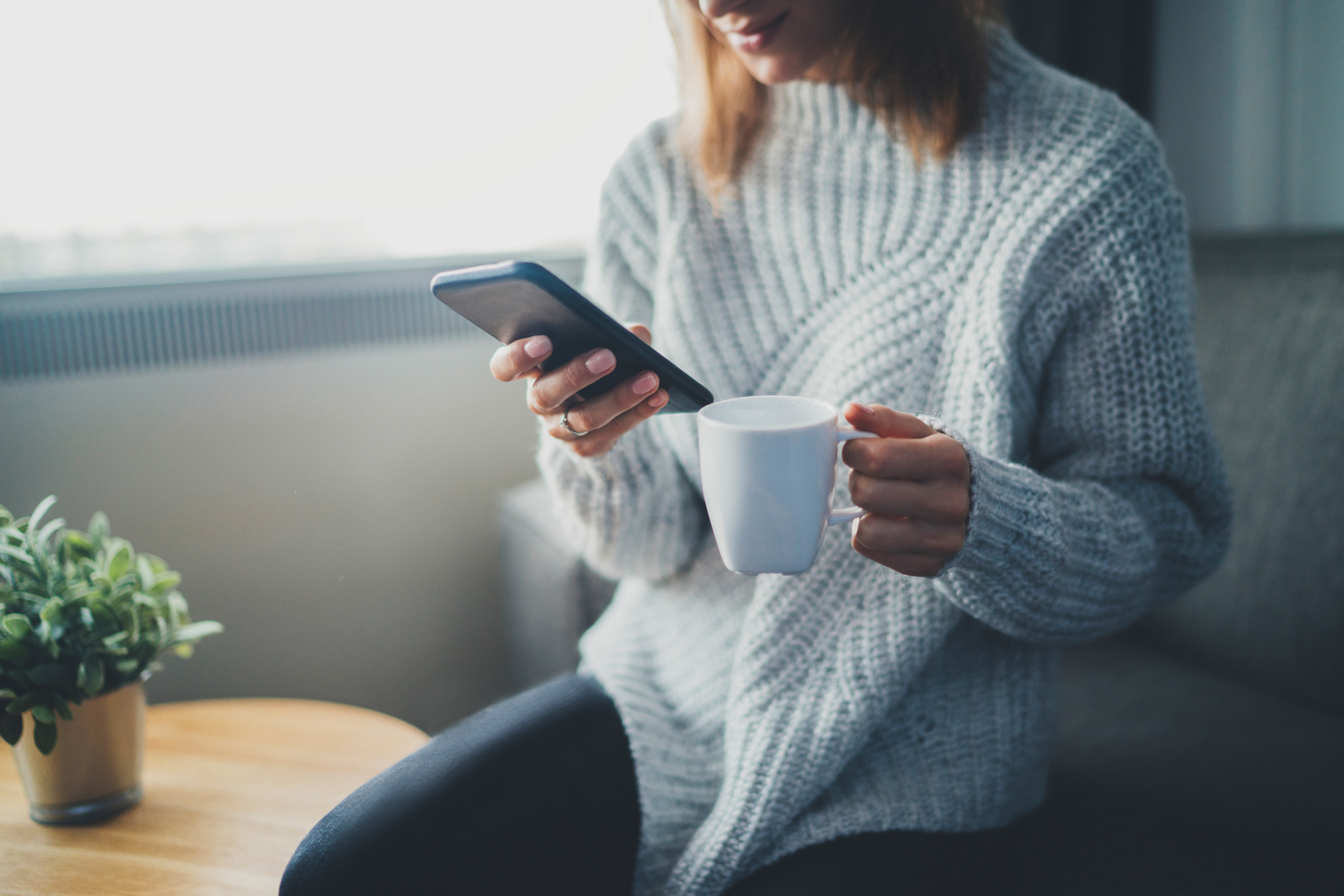 Kvinna som sitter med en kopp kaffe och surfar på mobilen