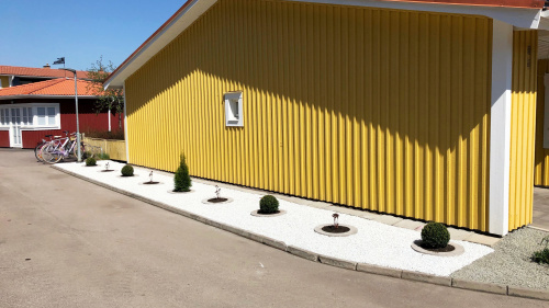 Rabatt med vit sten och buskar mot en gul fasad