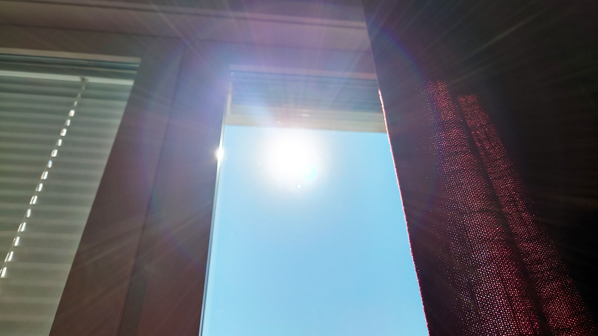 Sol genom ett fönster med persienner och gardiner